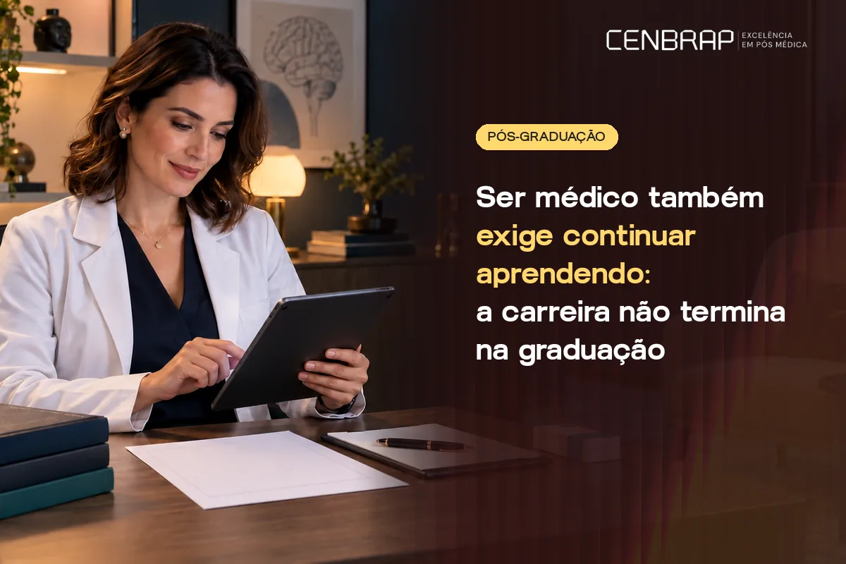 Médica de jaleco branco, sentada à mesa do consultório, sorri enquanto usa um tablet, com livros e papéis à frente.