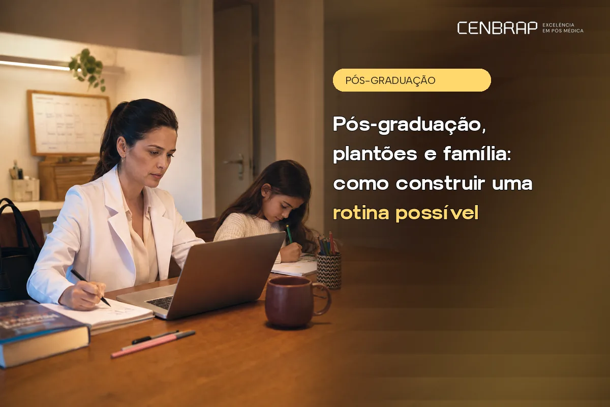 Médica de jaleco estuda à mesa de casa com notebook e caderno enquanto a filha faz a lição ao lado, no fim da tarde.